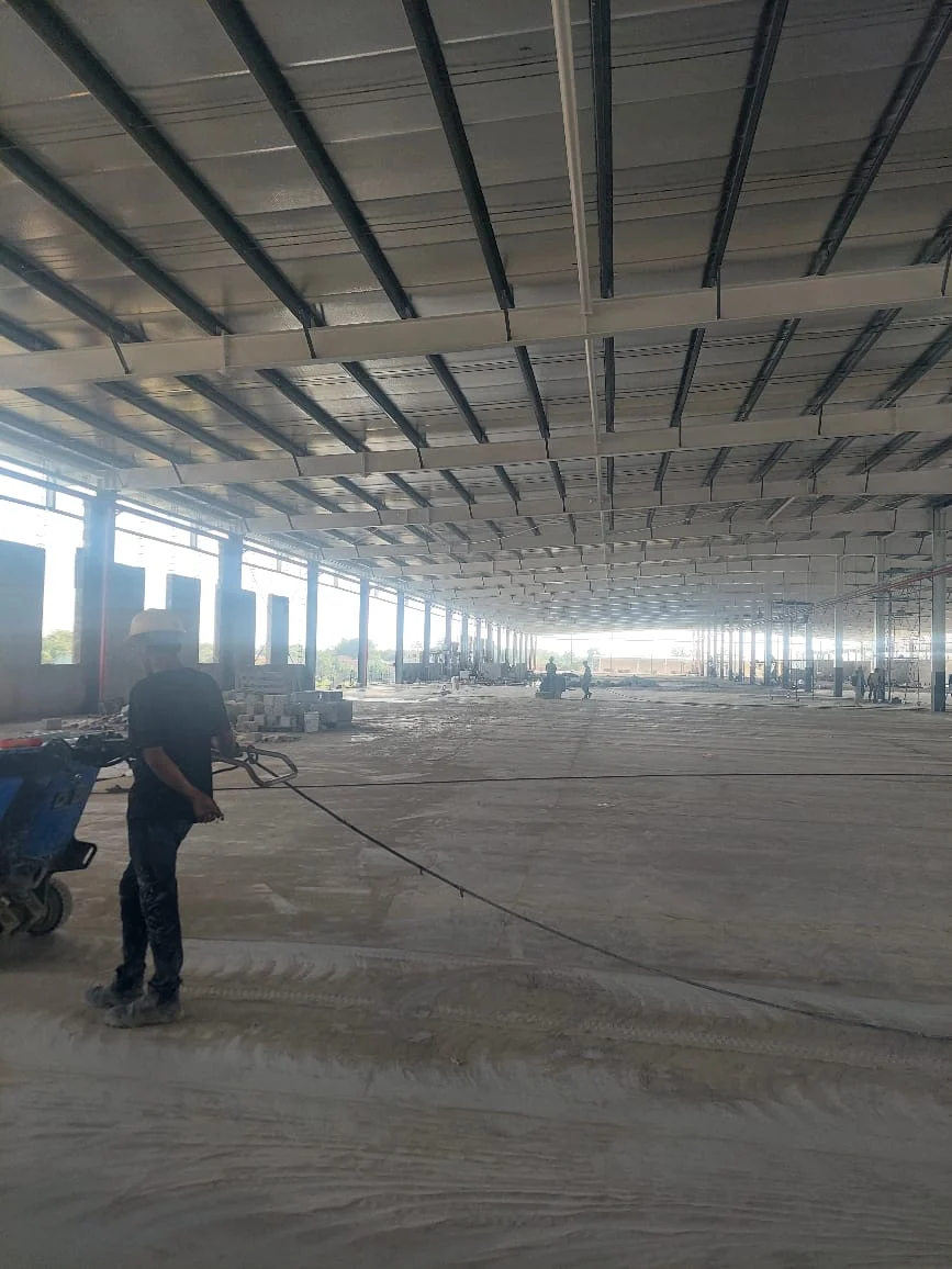 Dokumentasi pengerjaan epoxy lantai: aplikator menyelesaikan lapisan akhir di lantai beton area komersial.